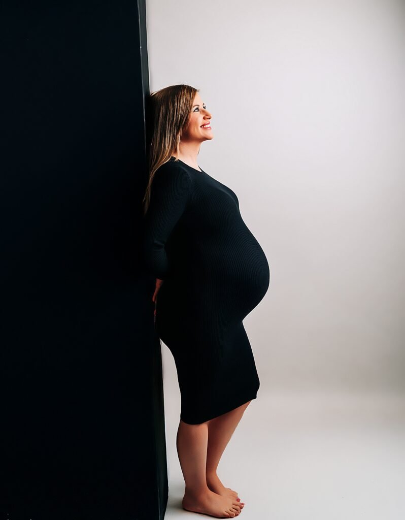 Sesión de fotos de embarazo en estudio en Jerez con fondo blanco y pared negra, futura mamá en perfil