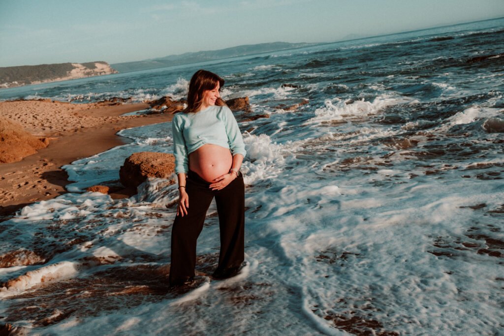 Primer plano de barriga de embarazada en entorno natural de dunas en Cádiz.