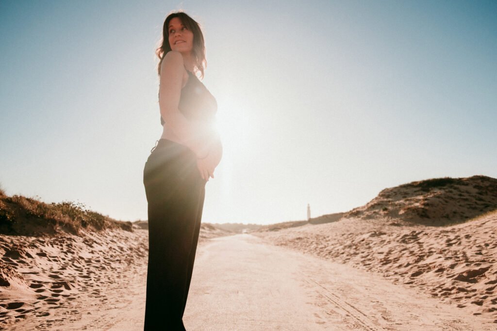 Primer plano de barriga de embarazada en entorno natural de dunas en Cádiz.